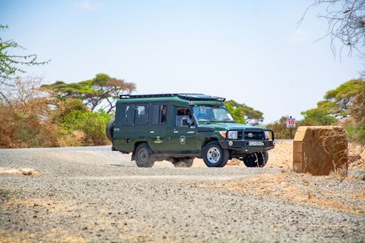 Green safari vehicle driving on rugged savannah road with scenic African landscape.